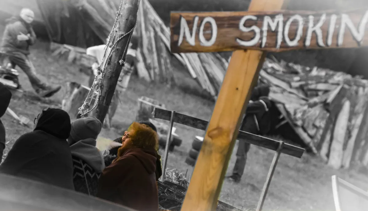 Wooden NO SMOKING sign hanging above an outdoor scene with seated smokers